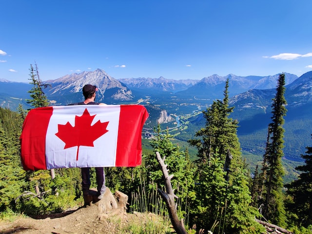 photo of a man holding a Canadian flag behind his back standing in front of mount Sulphur 