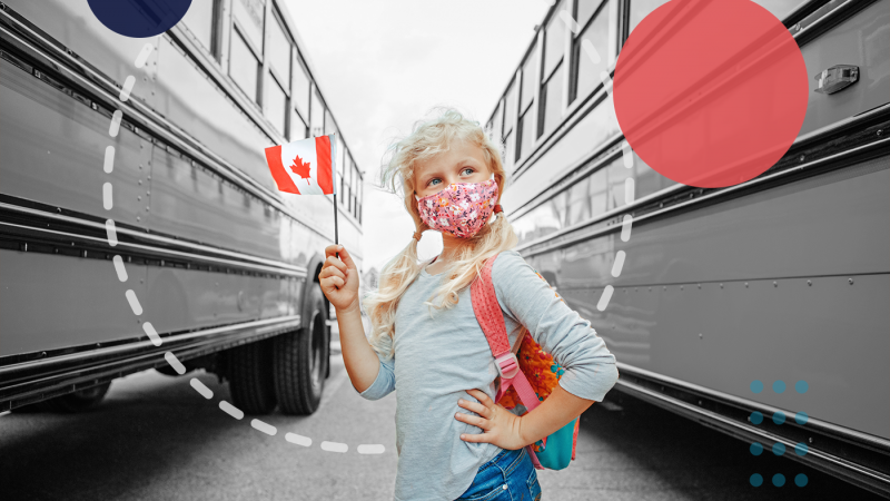 Young school girl holding a Canadian flag, wearing a medical mask and standing in front of two school buses 