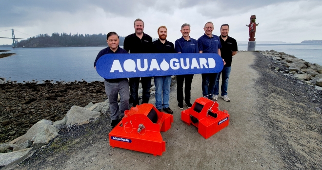 People holding an Aquaguard banner in front of a body of water 