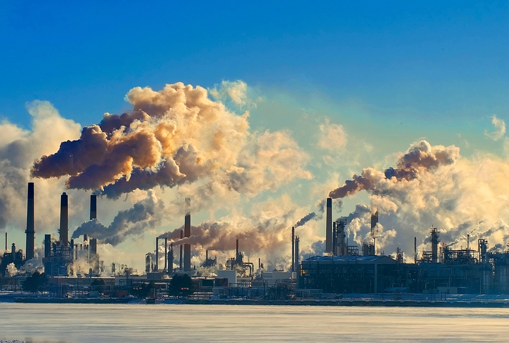An industrial complex with multiple smokestacks emitting thick clouds of smoke into the sky. 