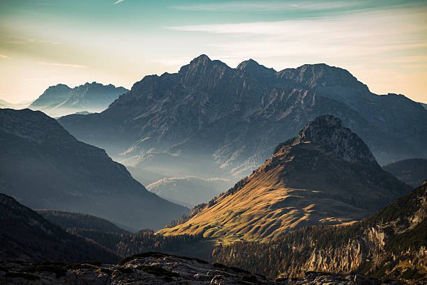 Sunrise over misty mountain peaks with a sunlit grassy slope in the foreground 