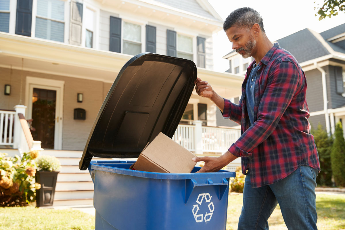 male putting a cardboard box in a recycling bin