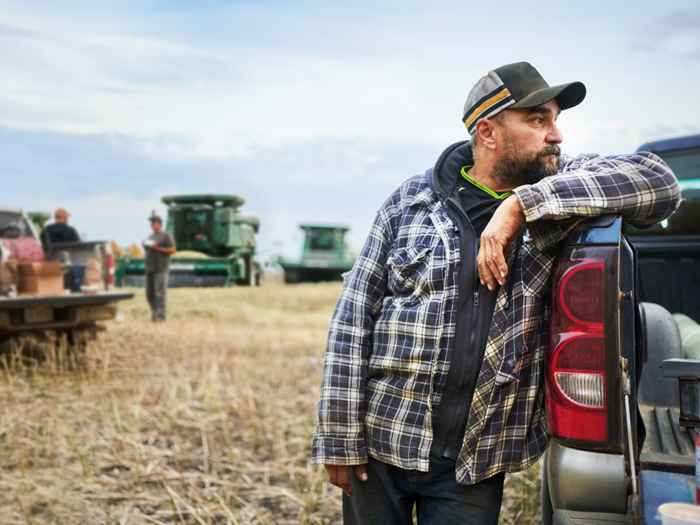 Male farmer leaning up against a truck in a farm field